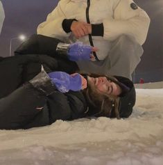 two people sitting in the snow with one holding something