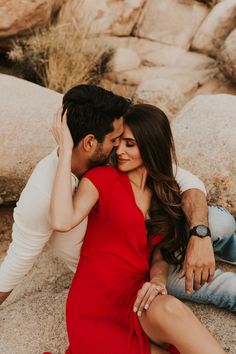 a man and woman sitting next to each other on the ground in front of rocks