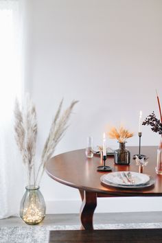 a wooden table topped with two vases filled with flowers and candles next to a window