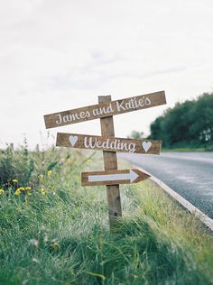 a wooden sign that says james and kate's wedding next to a road with yellow flowers