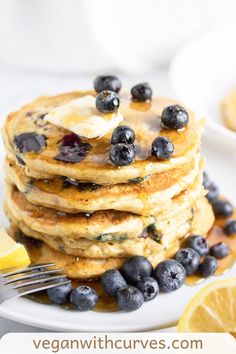 a stack of pancakes with blueberries and butter on top, next to a lemon wedge