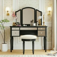 a dressing table with mirror, stool and vase on it in front of a white wall