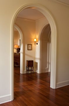 an arch in the middle of a hallway leading to another room with hardwood floors and white walls