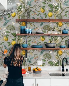 a woman standing in front of a kitchen counter with bowls and plates on the shelves