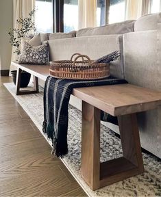 a basket sitting on top of a wooden bench in front of a couch next to a window