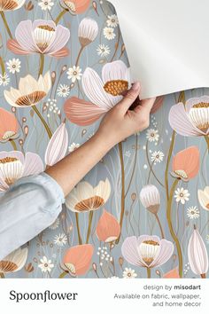 a woman's hand holding a piece of paper over a floral wallpaper design