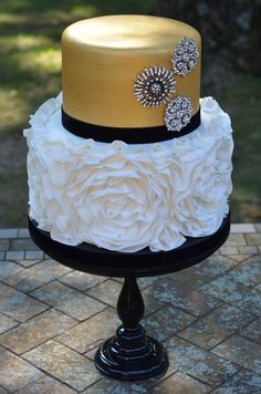 a three tiered cake with gold and white frosting on top, decorated with flowers