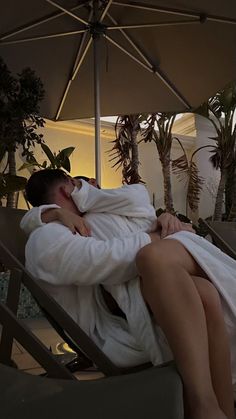 a woman wrapped in a towel laying on top of a beach chair under an umbrella