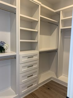 an empty walk in closet with white shelves and drawers on one side, wood floors