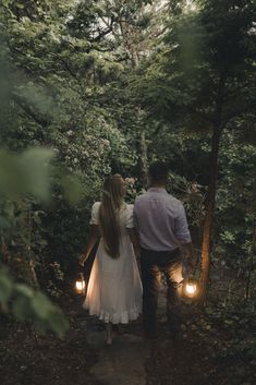 a man and woman walking through the woods holding hands with two lights on each hand