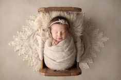 a newborn baby is wrapped in a blanket and sleeping on a sled with her hands under her chin