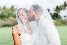 a bride and groom kissing under a veil in front of palm trees on their wedding day