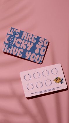 two small business cards sitting next to each other on top of a pink tablecloth