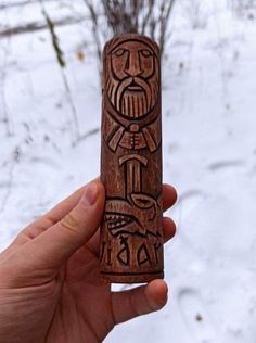 a person holding up a carved wooden object in front of snow covered trees and bushes