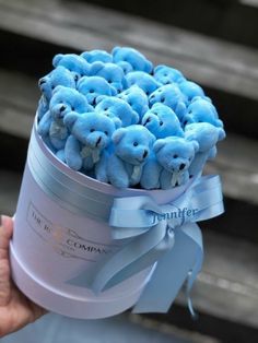 a person holding a blue teddy bear in a round container with ribbon around the top