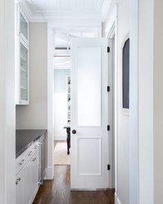 an open door leading to a kitchen with white cabinets and wood flooring on either side