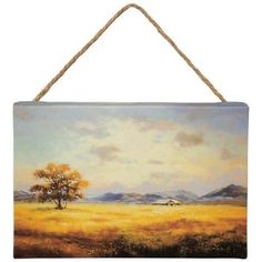 a painting hanging on a rope with a tree in the foreground and mountains in the background