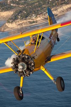 a small yellow airplane flying over the ocean