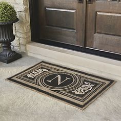 a door mat with the letter n on it next to a planter and two doors