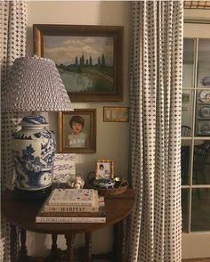 a table with books and a lamp on it in front of a window covered by curtains