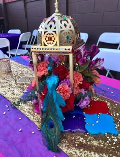 a table topped with a birdcage filled with flowers and a peacock tail sitting on top of it