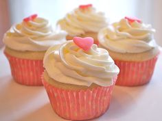 three cupcakes with white frosting and pink icing on top are sitting on a table