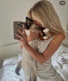 a woman holding a cat and taking a selfie with her cell phone in bed