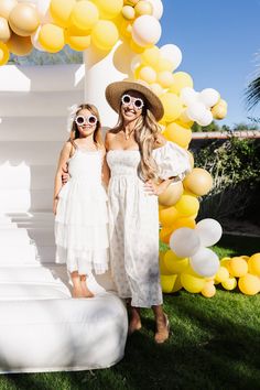 two women standing next to each other in front of yellow and white balloons