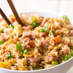 a bowl filled with rice, ham and green onions next to wooden chopsticks