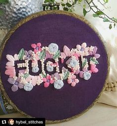 there is a purple embroidered sign with flowers on it and the word stitch spelled out