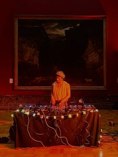 a man sitting at a table in front of a painting with lights strung across it