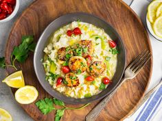 a bowl filled with pasta and shrimp on top of a wooden plate next to lemon wedges