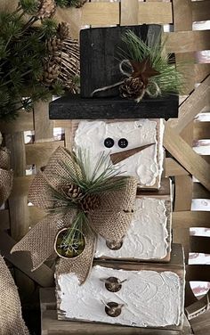 a snowman made out of boxes with pine cones on top and two small plants in the middle