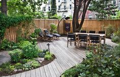 a wooden deck surrounded by plants and trees with chairs around the table in the middle