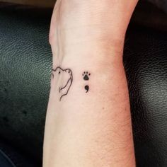 a small tattoo on the wrist of a person with a dog's paw and footprints