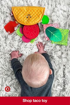 a baby laying on the floor next to toys that are shaped like fruits and vegetables