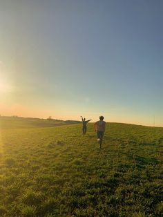 two people are walking in the grass with their arms out to each other as the sun sets