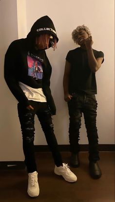 two young men standing next to each other in front of a wall wearing black and white clothing