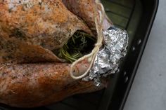 a whole turkey wrapped in tin foil and sitting on top of an oven rack with some herbs