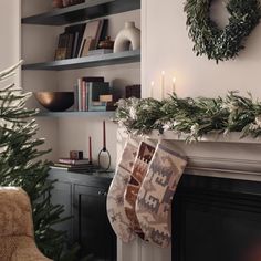 christmas stockings hanging from the fireplace mantel in front of a wreath and bookshelf