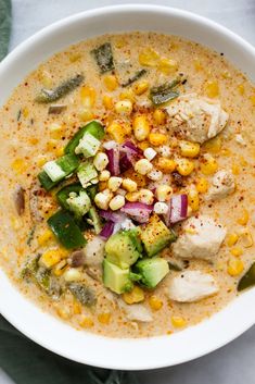 a white bowl filled with chicken, corn and avocado on top of a table