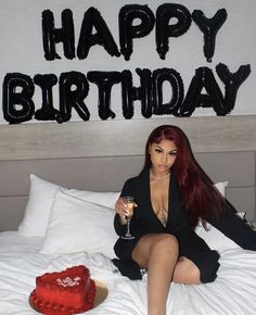 a woman sitting on top of a bed holding a wine glass in front of a birthday cake