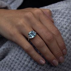 a woman's hand wearing a ring with an aqua blue topazte on it