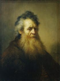 an old man with a long beard and wearing a black coat is looking at the camera