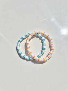 two bracelets with multicolored beads on a white surface, one is in the shape of a circle