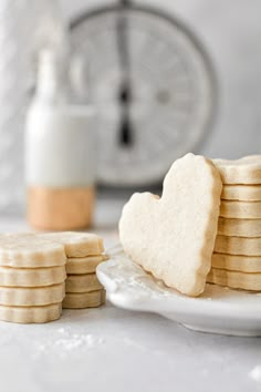 a stack of heart shaped shortbread cookies on a white plate next to a clock