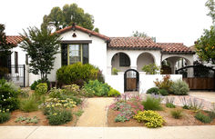 a white house with lots of plants and flowers around it's front entrance area