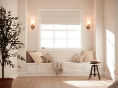 a white window seat with pillows on it and a potted plant in the corner