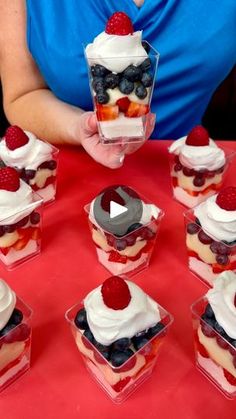 cupcakes with whipped cream and berries are arranged on a red tablecloth in front of a woman's face