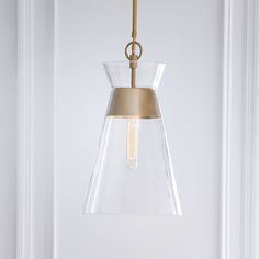 a glass and brass pendant light hanging from a ceiling fixture in a white walled room